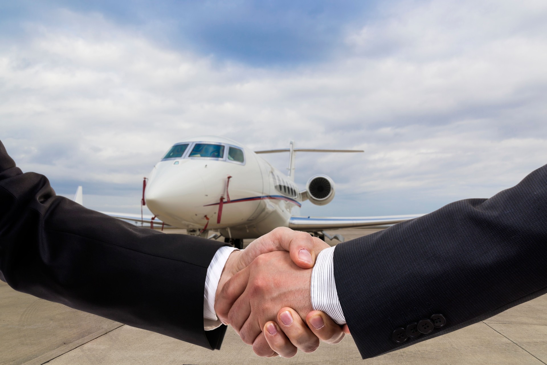 Businessmen shaking hands in front of corporate jet